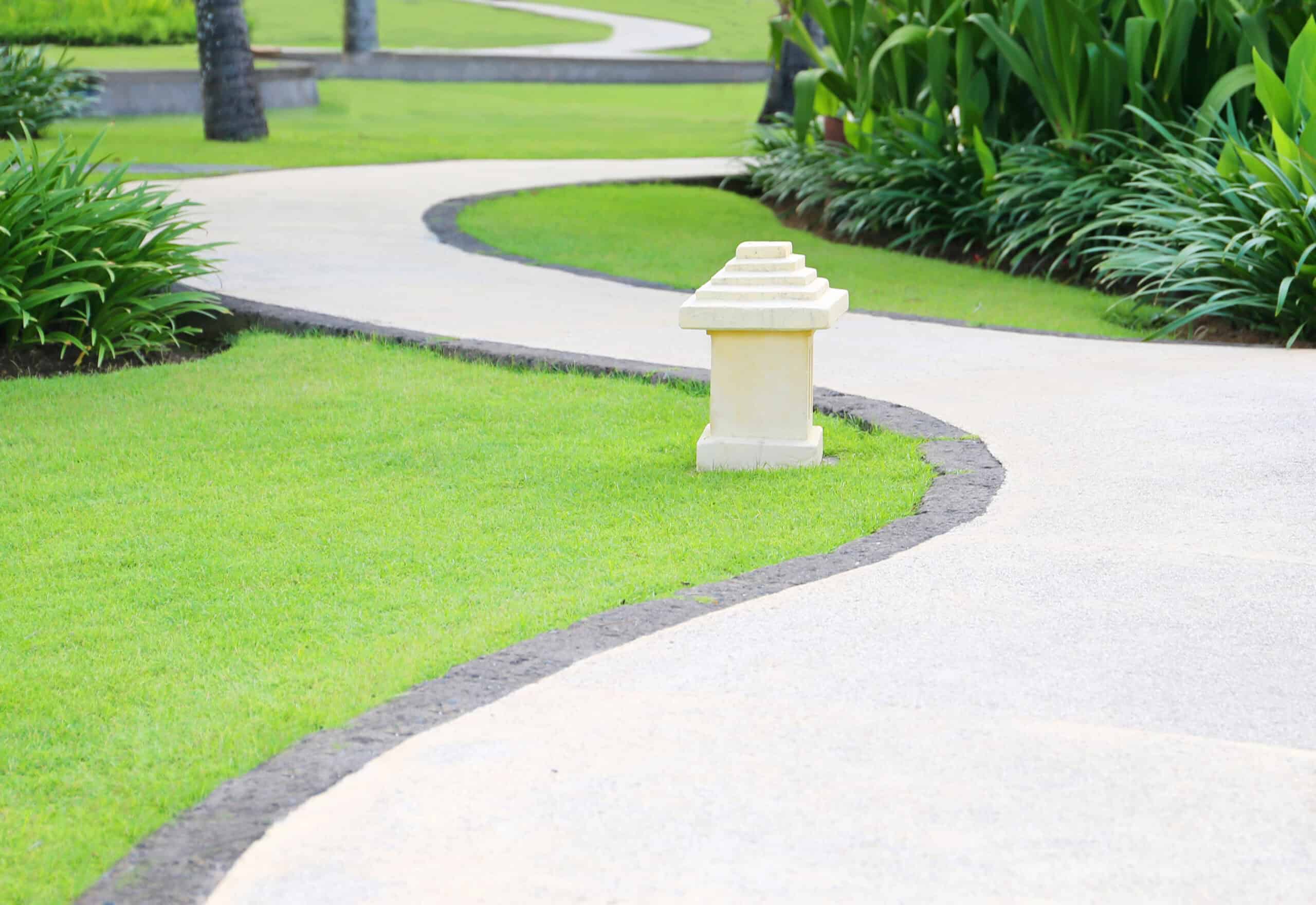 A winding stone path bordered by lush grass and vibrant plants curves around a small decorative stone lantern in a meticulously maintained garden, showcasing the essence of expert lawn care.