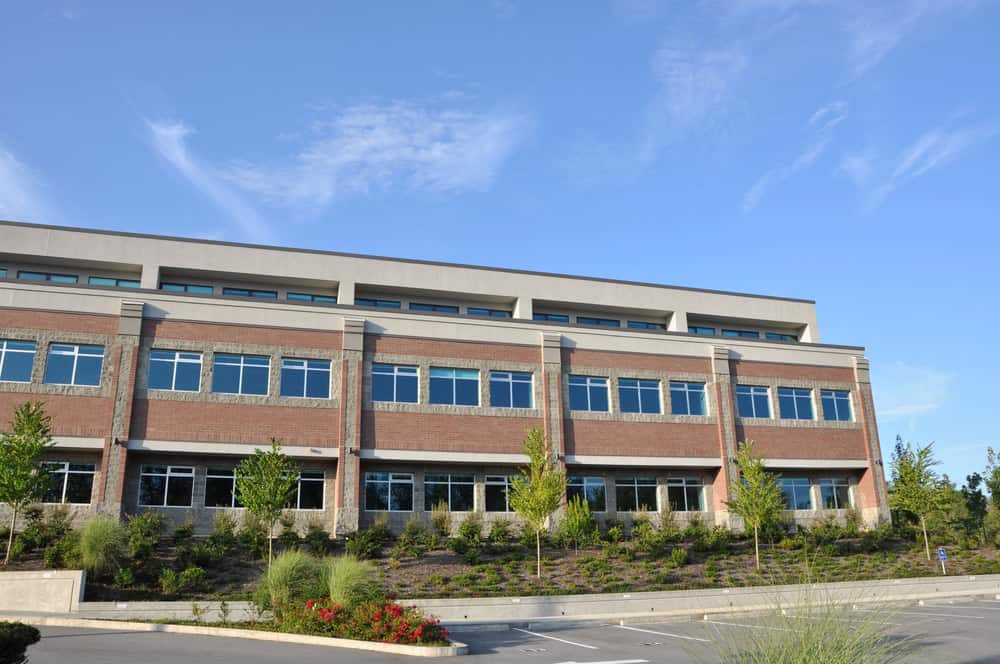A modern two-story office building with large windows, surrounded by landscaped greenery and an empty parking lot under a clear blue sky, benefits from expert commercial pest control to ensure a pristine environment.