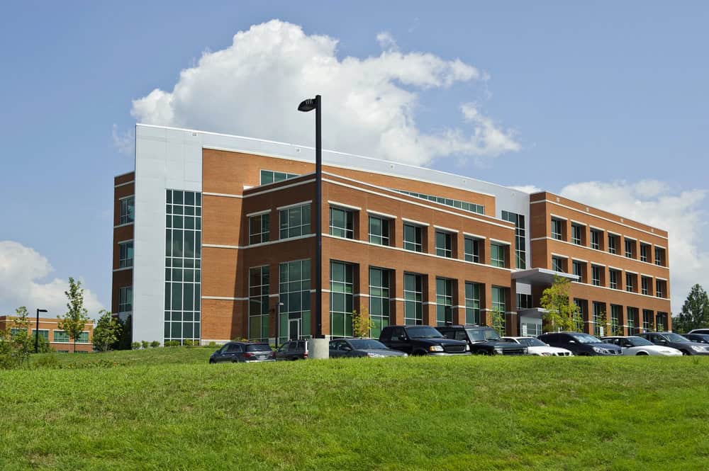 A modern office building with large windows is surrounded by a meticulously maintained green lawn, reflecting expert lawn care. Several cars are parked in front, highlighting the site's accessibility.