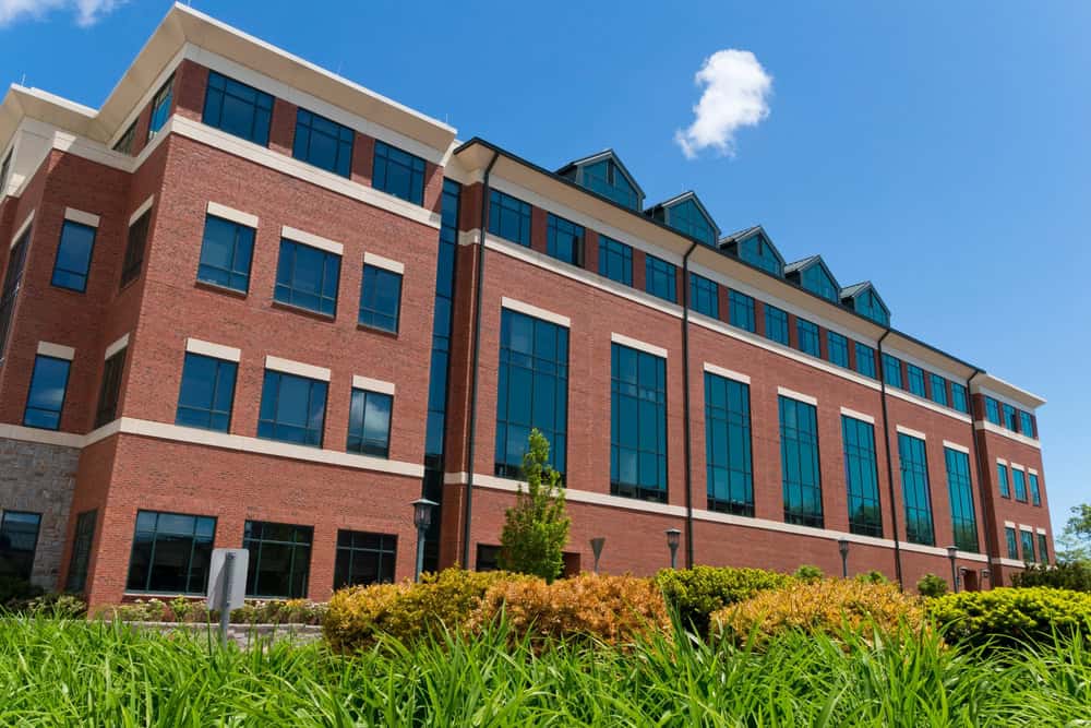 A large brick office building with numerous windows, surrounded by green landscaping under a clear blue sky, benefits from discreet commercial pest control to ensure a peaceful and clean environment for its occupants.