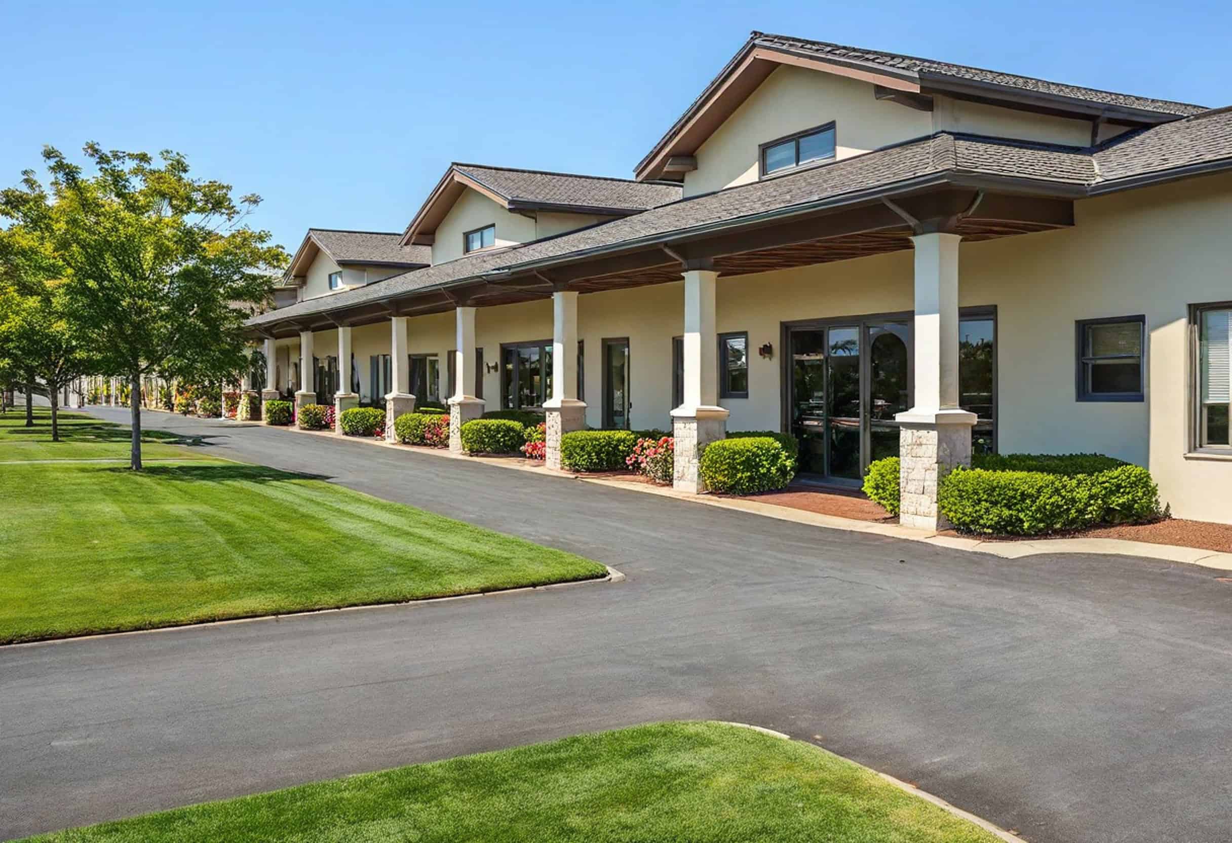 A long building with multiple arches, enveloped by meticulously maintained green lawns and trees, stands gracefully under a clear blue sky-a perfect example of exquisite retail landscaping.