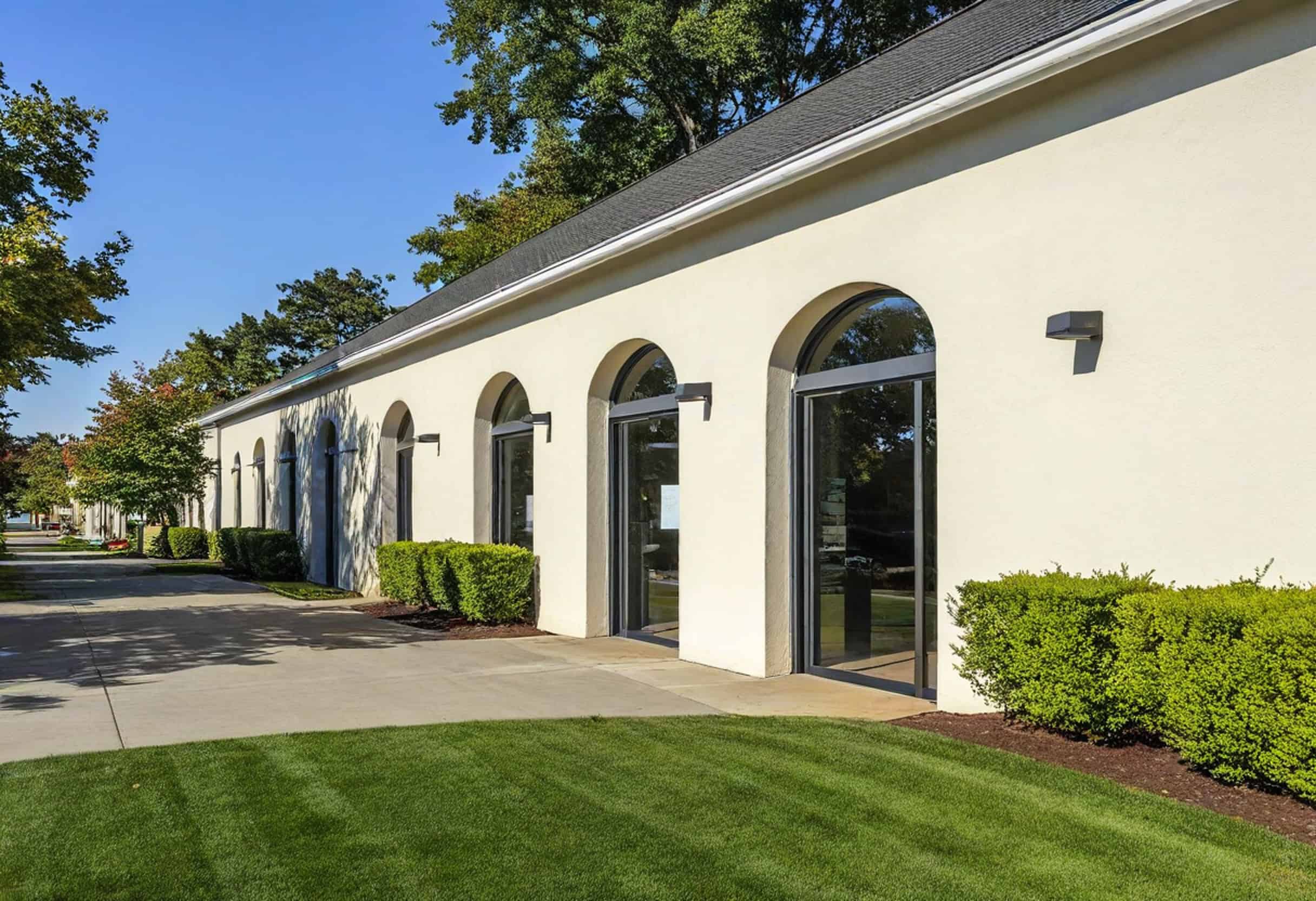 A long beige building with arched windows, surrounded by expertly designed retail landscaping and a well-maintained lawn, all under a clear blue sky.
