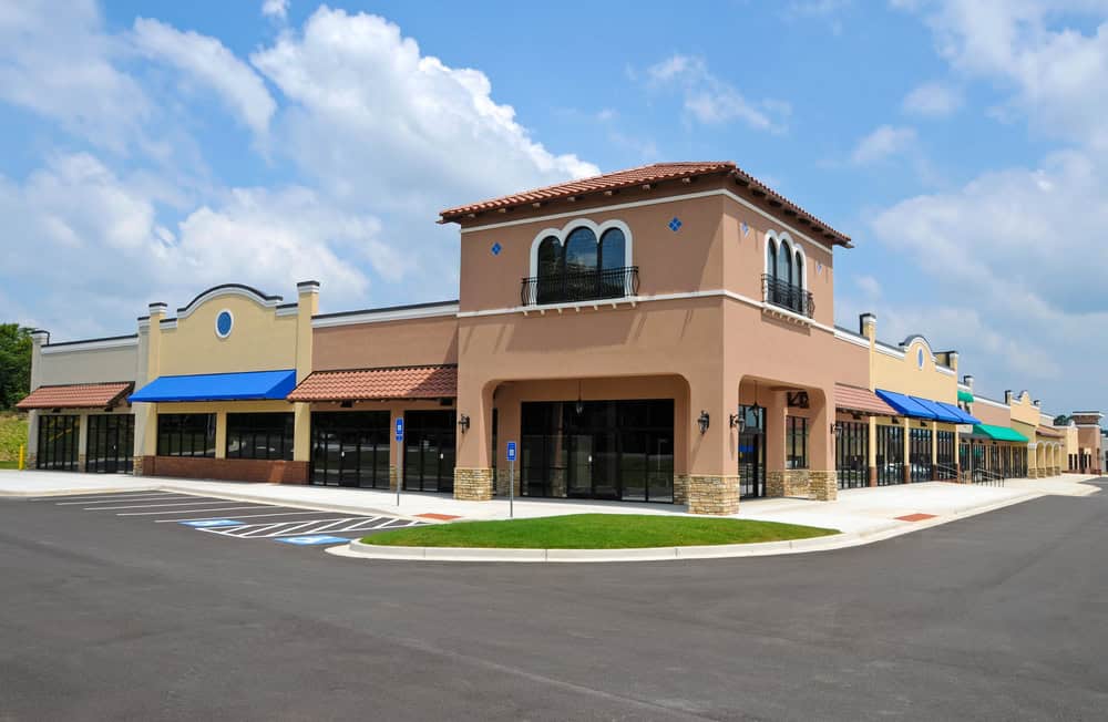 A vacant strip mall with multiple storefronts and colorful awnings under a partly cloudy sky awaits vibrant retail landscaping to breathe new life into the scene.