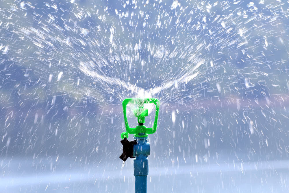 A green lawn sprinkler sprays water outward in all directions, creating a misty pattern against a blurred outdoor background—perfect inspiration for your next blog post or template design.